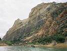 A group of rafts moving down the Green River toward a steep cliff face in the distance