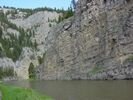 Flat brown river flowing past a vertical gray cliff face