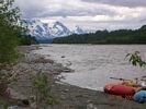 Red and blue rafts pulled up on gravel bar, with glaciers and mountains in the distance. Gray, overcast day.