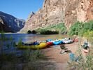 Bright yellow, red, and blue rafts on shore in the morning light with the Grand Canyon backdrop